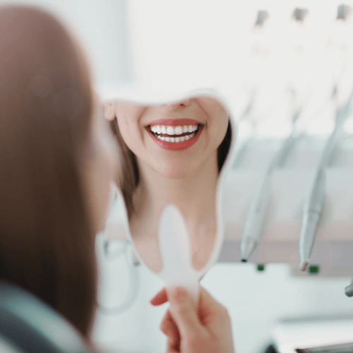 Patient admiring her bright smile after teeth whitening treatment.
