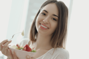 Young woman smiling while eating a fresh salad, demonstrating healthy eating habits for dental health