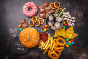 An assortment of unhealthy foods and drinks, including sugary sweets, soda, and fast food.