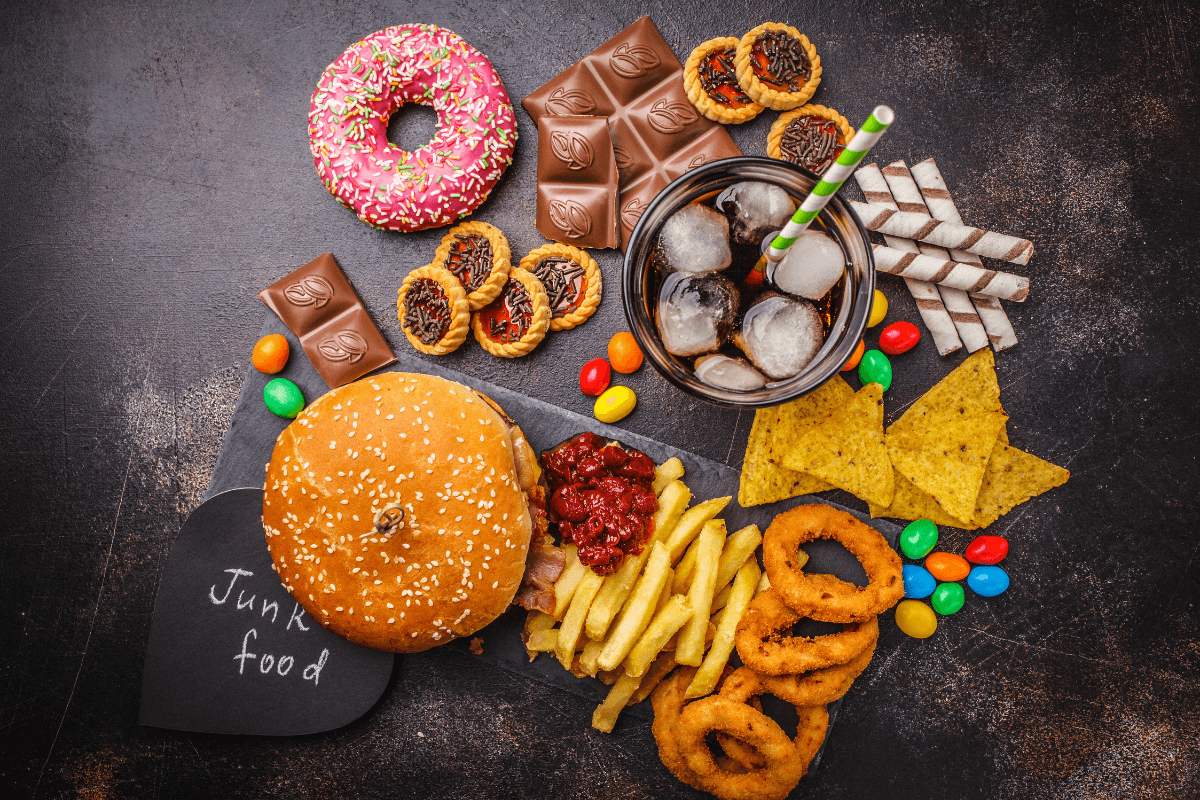 An assortment of unhealthy foods and drinks, including sugary sweets, soda, and fast food.