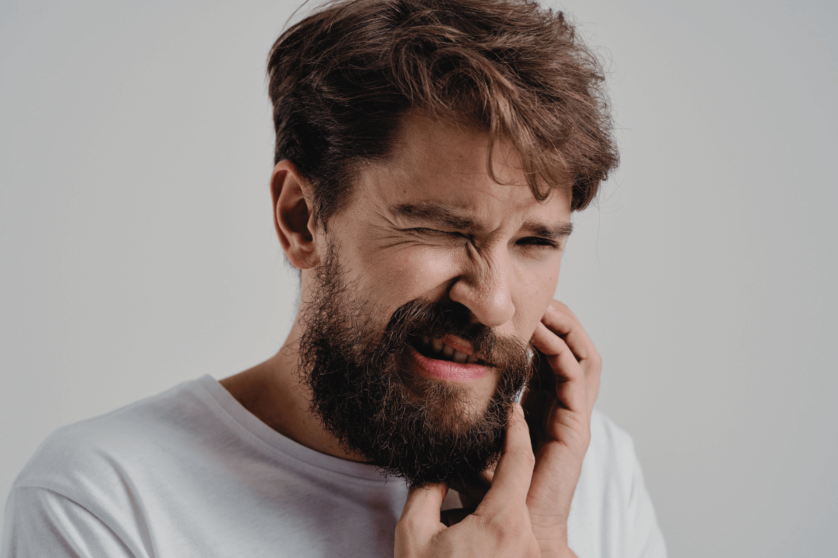 Young man in holding his cheek in pain, indicative of a dental emergency.