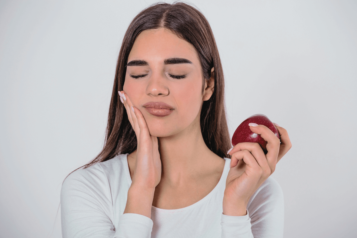 Woman holding an apple and experiencing tooth sensitivity pain