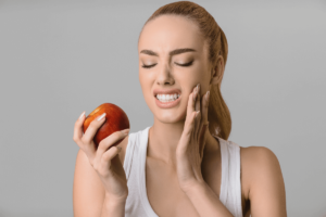 Woman holding an apple and experiencing tooth sensitivity pain