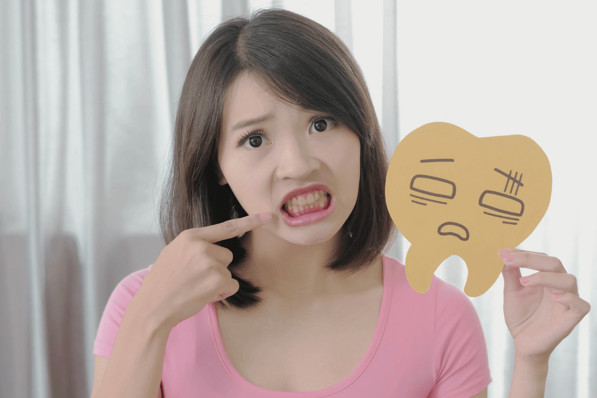 Woman showing displeasure while pointing at her teeth, holding a tooth cartoon with frustrated expression symbol.