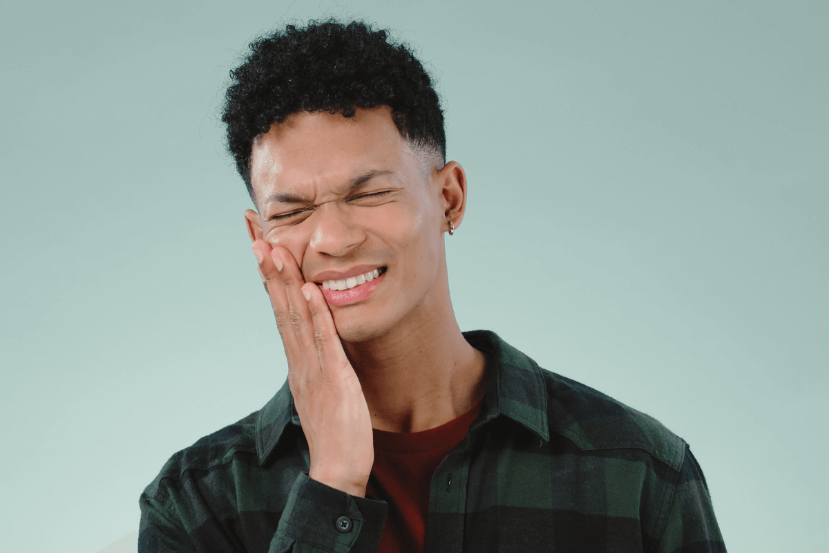 Young man in plaid shirt holding his cheek in pain, indicative of a dental emergency.