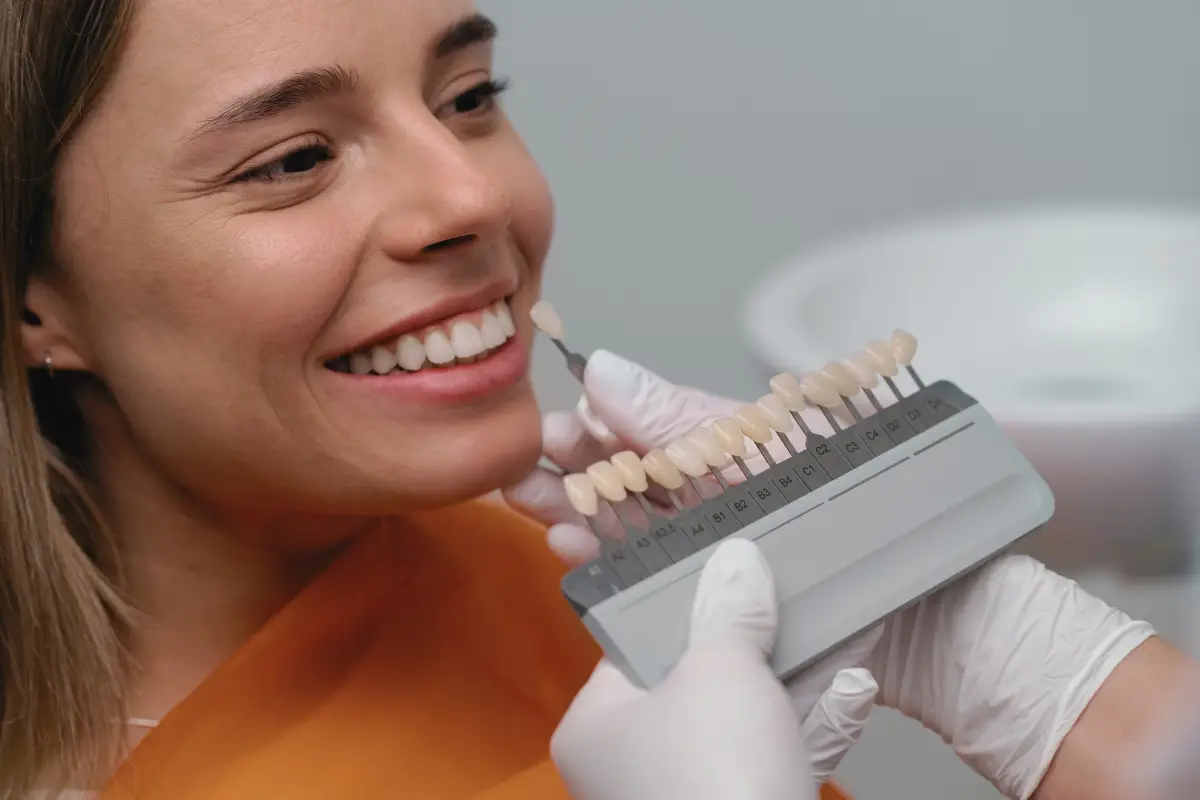 Dentist matching dental crown color to female patient’s teeth